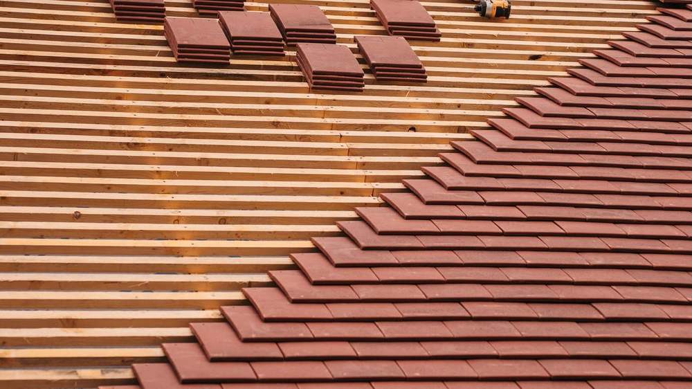 Couvreur posant des tuiles en terre cuite sur une toiture en cours de rénovation